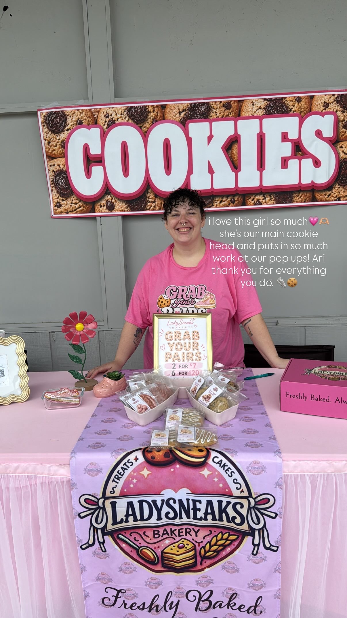 Ari smiling behind the pink LadySneaks Bakery table at a cookie pop up